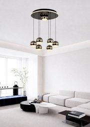 Moderne LED-Pendelleuchte mit sechs kugelförmigen Lampen, hängend von einer runden Deckenplatte in einem stilvollen Wohnzimmer, seitliche Perspektive.