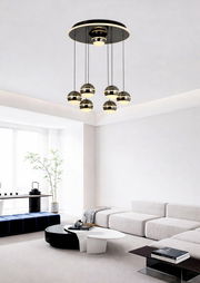 Moderne LED-Pendelleuchte mit sechs kugelförmigen Lampen, hängend von einer runden Deckenplatte in einem stilvollen Wohnzimmer, seitliche Perspektive.