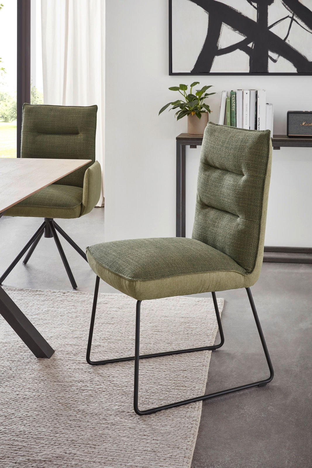 Grüner Stuhl mit gepolsterter Rückenlehne und Metallbeinen, seitliche Perspektive