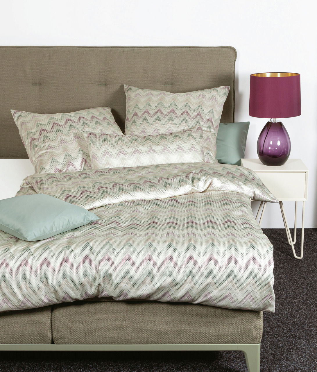 Bett mit Mako-Satin Bettwäsche in Zickzack-Muster, Perspektive von vorne, mit lila Lampe auf Nachttisch.