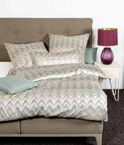 Bett mit Mako-Satin Bettwäsche in Zickzack-Muster, Perspektive von vorne, mit lila Lampe auf Nachttisch.