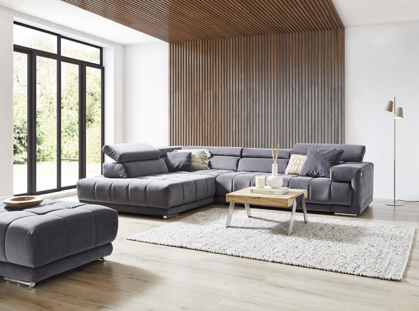 Graues Ecksofa in modernem Wohnzimmer mit Holzverkleidung und großen Fenstern, seitliche Perspektive