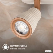 Nahaufnahme eines modernen LED-Deckenstrahlers/Spots mit geriffeltem, weißem Lampenkopf und kupferfarbenem Ring, Perspektive: schräg von unten auf die Frontlinse