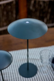 Moderne, ronde staande lamp in mat donkergrijs met een slanke voet en een platte, schijfvormige kap, van bovenaf licht schuin gefotografeerd.