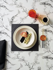 Vogelperspektive auf einen Teller aus dem Tellerset Eclipse Day, platziert auf einem dunklen Untersetzer mit asiatischem Essen, umgeben von einem roten Glas, einer kleinen weißen Schale und Essstäbchen auf einem kunstvoll gemusterten Tisch.