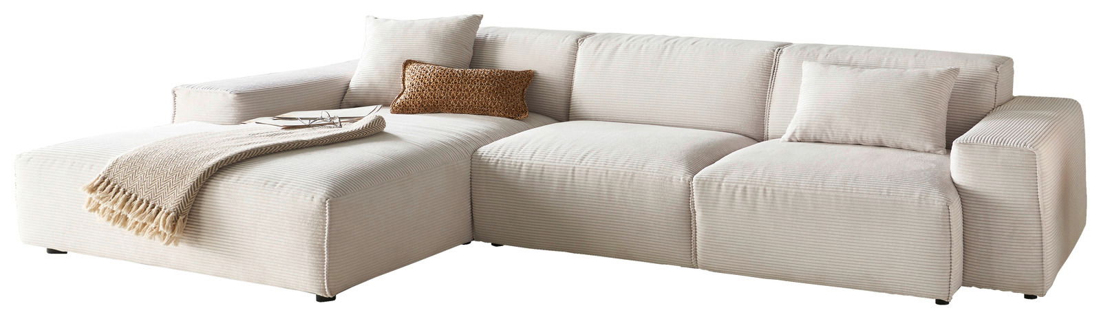 Beige Ecksofa mit Ottomane links, dekoriert mit Kissen und Decke, seitliche Perspektive.