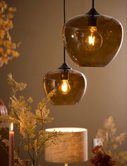 Zwei hängende Leuchten mit bernsteinfarbenen Glaskugeln, die warmes Licht spenden, aus einer seitlichen Perspektive fotografiert.