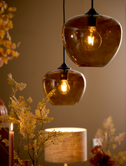 Zwei hängende Leuchten mit bernsteinfarbenen Glaskugeln, die warmes Licht spenden, aus einer seitlichen Perspektive fotografiert.