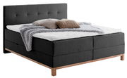Boxspringbett in dunklem Stoff mit hohem Kopfteil, dekoriert mit Kissen und Decke, seitliche Perspektive