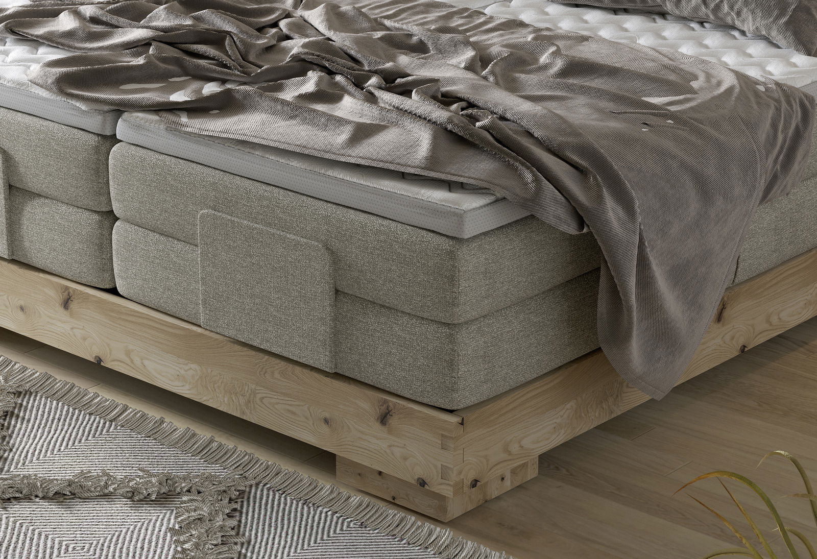 Nahaufnahme eines Boxspringbetts mit grauem Stoffbezug und Holzrahmen, von der Seite betrachtet.