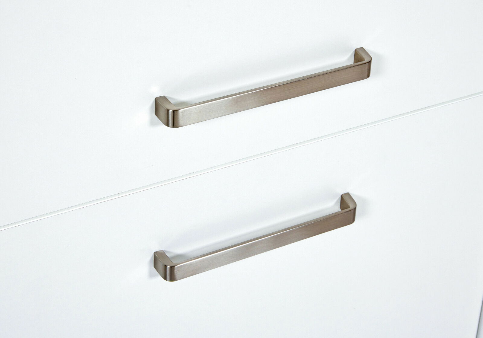 Nahaufnahme von zwei modernen, silbernen Griffen an weißen Schranktüren, perspektivisch von vorne betrachtet.