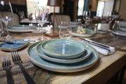 Blau-grünes Keramik-Tellerset mit drei gestapelten Tellern auf gedecktem Holztisch im Restaurant, aufgenommen aus schräger Nahperspektive auf Tischhöhe