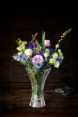 Kristallvase mit einem bunten Blumenstrauß, frontal fotografiert vor einem dunklen Hintergrund.