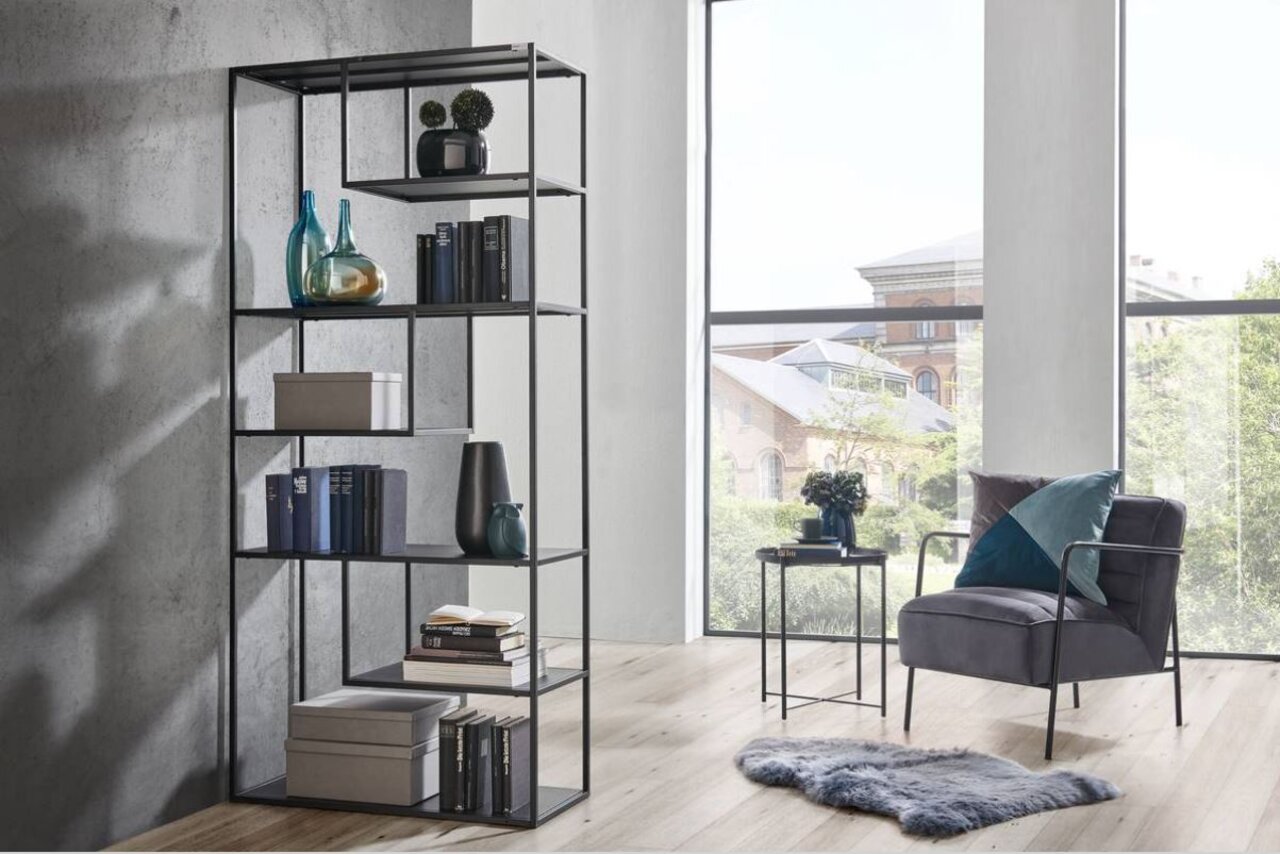 Modernes hohes Regal aus Metall mit mehreren Fächern, dekoriert mit Büchern und Vasen, in einem hellen Raum mit großen Fenstern, seitliche Perspektive.