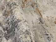 Nahaufnahme eines Designer-Teppichs mit abstraktem Muster in Grau-, Beige- und Brauntönen, aus seitlicher Perspektive aufgenommen.