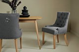 Zwei graue, gepolsterte Stühle mit Holzbeinen, einer von vorne und einer von hinten, an einem Holztisch in einem eleganten Esszimmer.