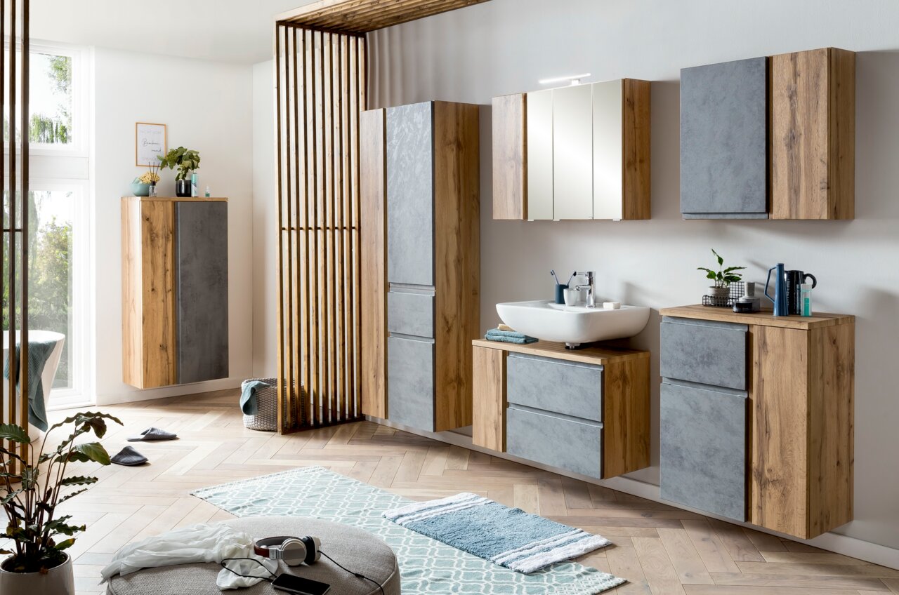 Moderner Waschbeckenunterschrank in Holzoptik mit grauen Fronten, rechts im Badezimmer platziert, aus seitlicher Perspektive fotografiert.