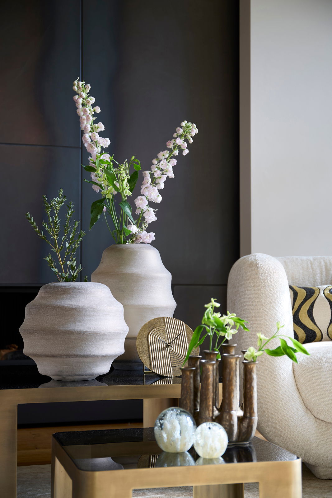 Moderne Wohnzimmerdekoration mit einer goldenen Uhr auf einem Tisch, umgeben von stilvollen Vasen und Pflanzen, seitliche Perspektive.