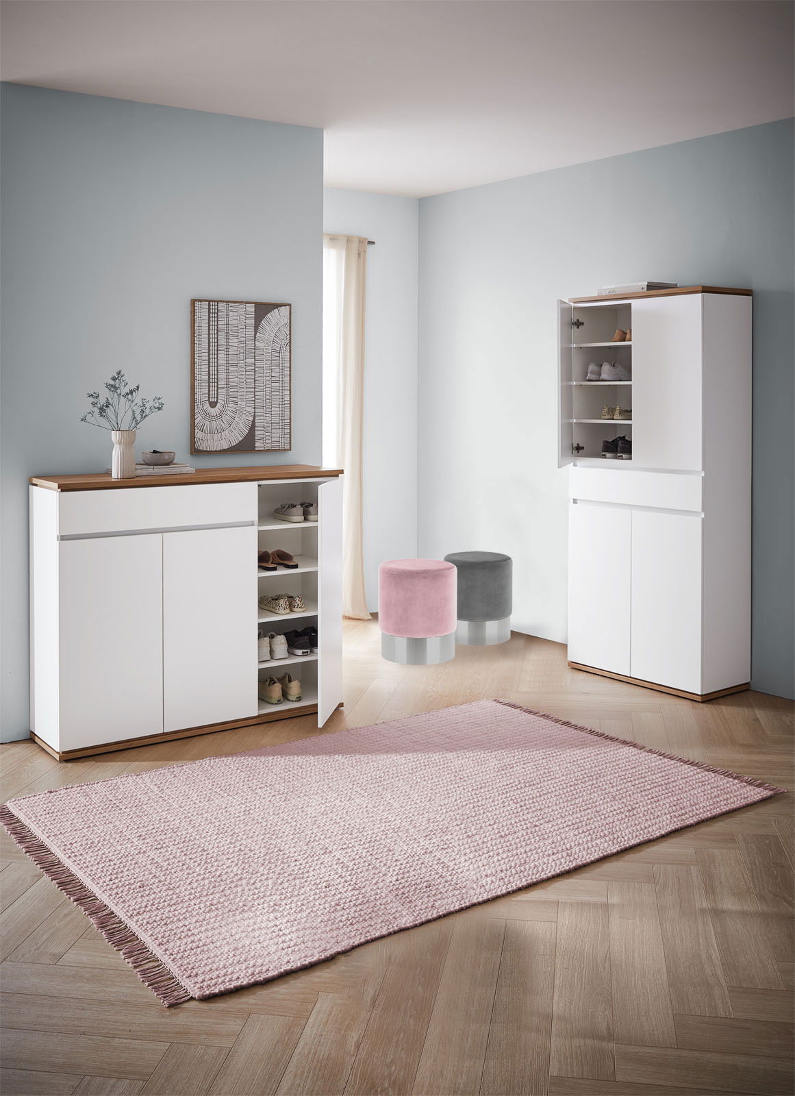 Moderner Eingangsbereich mit zwei weißen Schuhschränken, einem geöffneten, und zwei runden Hockern in Rosa und Grau, aus der Perspektive von vorne.