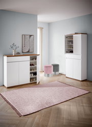 Moderner Eingangsbereich mit zwei weißen Schuhschränken, einem geöffneten, und zwei runden Hockern in Rosa und Grau, aus der Perspektive von vorne.