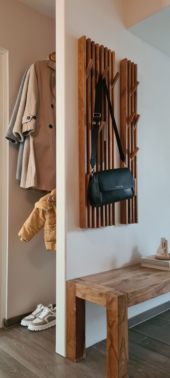 Holzgarderobenpaneel an der Wand mit Haken, an denen eine schwarze Tasche hängt. Perspektive von der Seite.