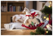 Weißes Schaukelpferd mit rotem Sattel und goldenen Details, seitliche Perspektive, dekoriert mit Geschenken und einem Weihnachtsbaum auf dem Sockel.