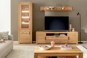 Moderne Wohnzimmeransicht mit einer beleuchteten Vitrine aus Holz, einem TV-Schrank und einem Couchtisch, alles in hellem Holzton. Perspektive von vorne.