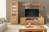 Moderne Wohnzimmeransicht mit einer beleuchteten Vitrine aus Holz, einem TV-Schrank und einem Couchtisch, alles in hellem Holzton. Perspektive von vorne.