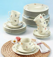 Koffieservies Marie-Luise, 18-delig, met bloemmotief, bestaande uit kopjes, schoteltjes en borden, op een tafel met een gevlochten onderlegger en bloemen, gefotografeerd vanuit vogelperspectief.