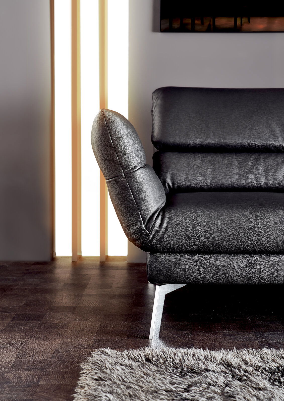 Nahaufnahme eines schwarzen Ledersofas mit verstellbarer Rückenlehne und Metallfüßen, seitliche Perspektive.