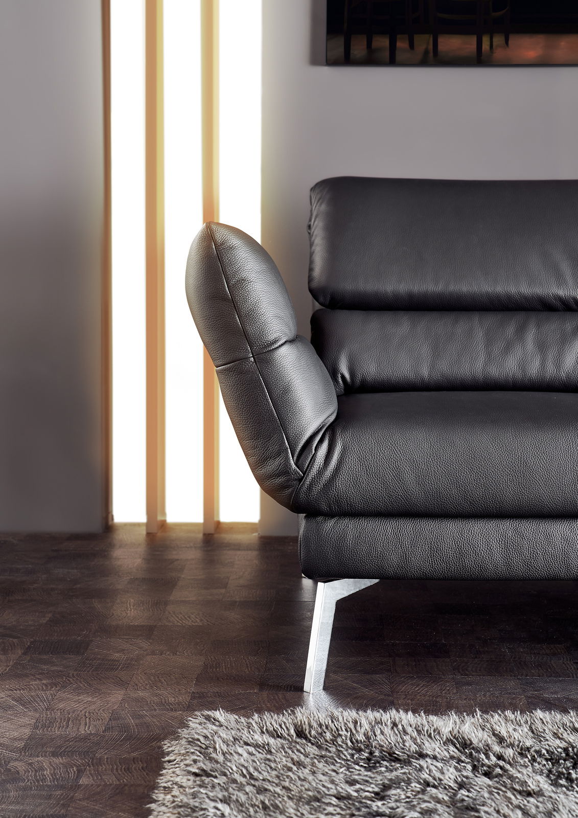 Nahaufnahme eines schwarzen Ledersofas mit verstellbarer Rückenlehne und Metallfüßen, seitliche Perspektive.