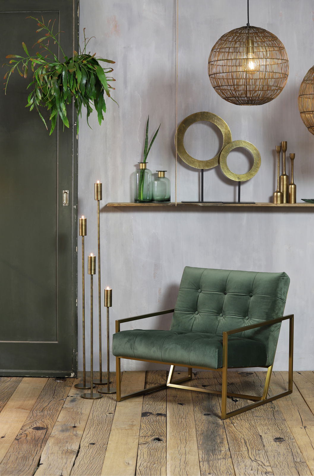 Ein stilvolles Wohnzimmer mit einem grünen Sessel aus Samt und goldenen Metallakzenten, umgeben von modernen Dekorationen wie hängenden Lampen und Pflanzen. Perspektive: Frontalansicht.