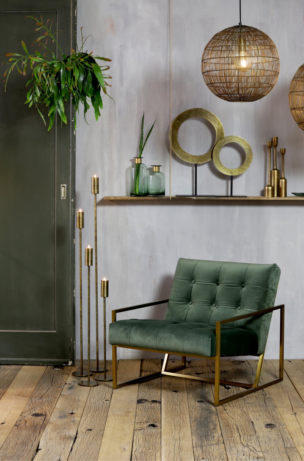 Ein stilvolles Wohnzimmer mit einem grünen Sessel aus Samt und goldenen Metallakzenten, umgeben von modernen Dekorationen wie hängenden Lampen und Pflanzen. Perspektive: Frontalansicht.