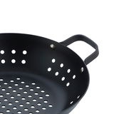 Nahaufnahme einer schwarzen BBQ Wokpfanne mit Löchern und Griffen, von oben betrachtet.