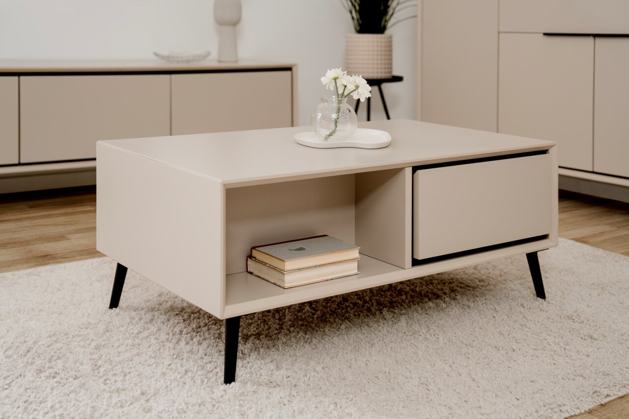 Beige Couchtisch mit schwarzem Gestell, dekoriert mit einer Vase und Büchern, aus seitlicher Perspektive fotografiert.