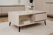 Beige Couchtisch mit schwarzem Gestell, dekoriert mit einer Vase und Büchern, aus seitlicher Perspektive fotografiert.