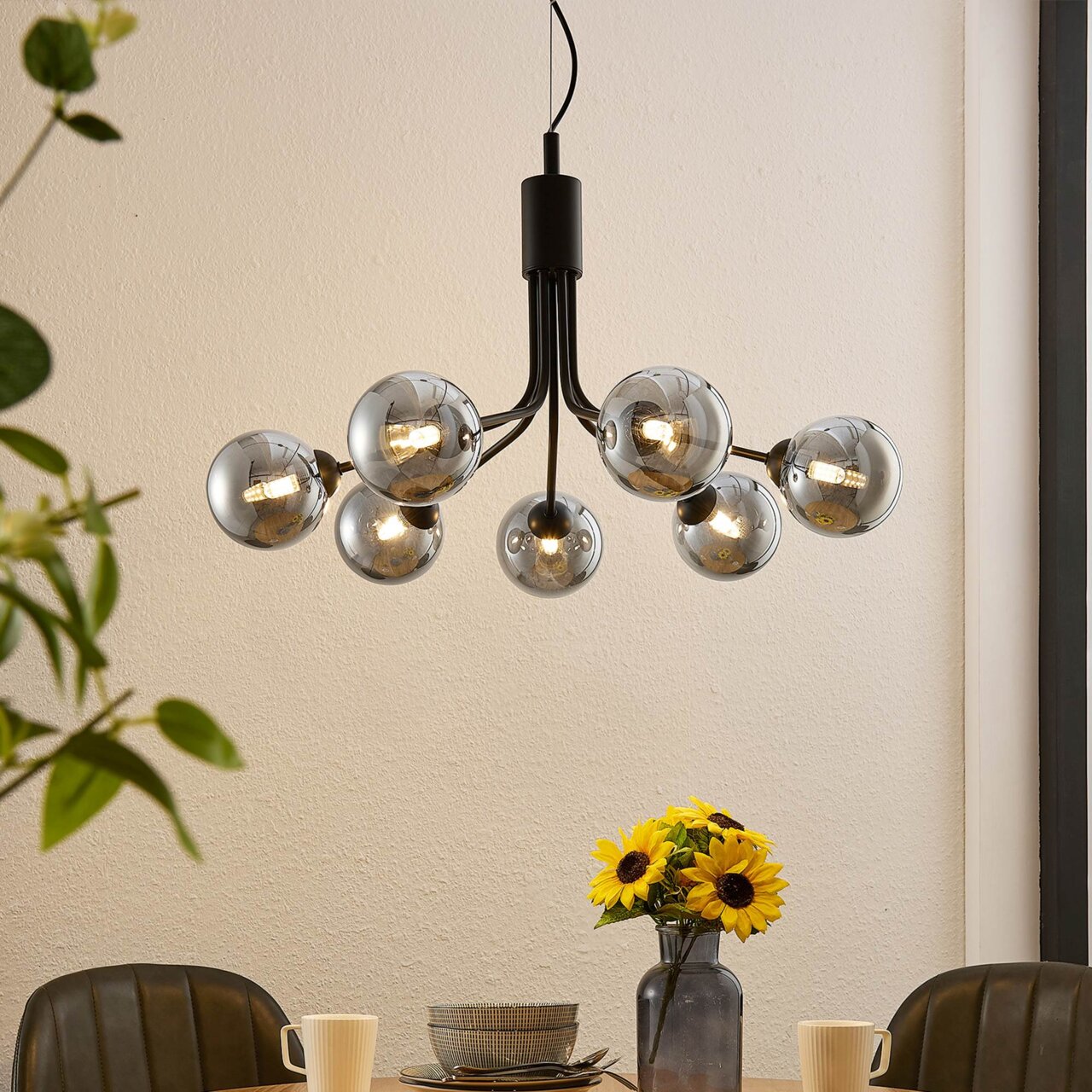Novel Hängeleuchte Moderne Hängeleuchte mit mehreren kugelförmigen Glühbirnen, von unten betrachtet, über einem Esstisch mit Sonnenblumen.