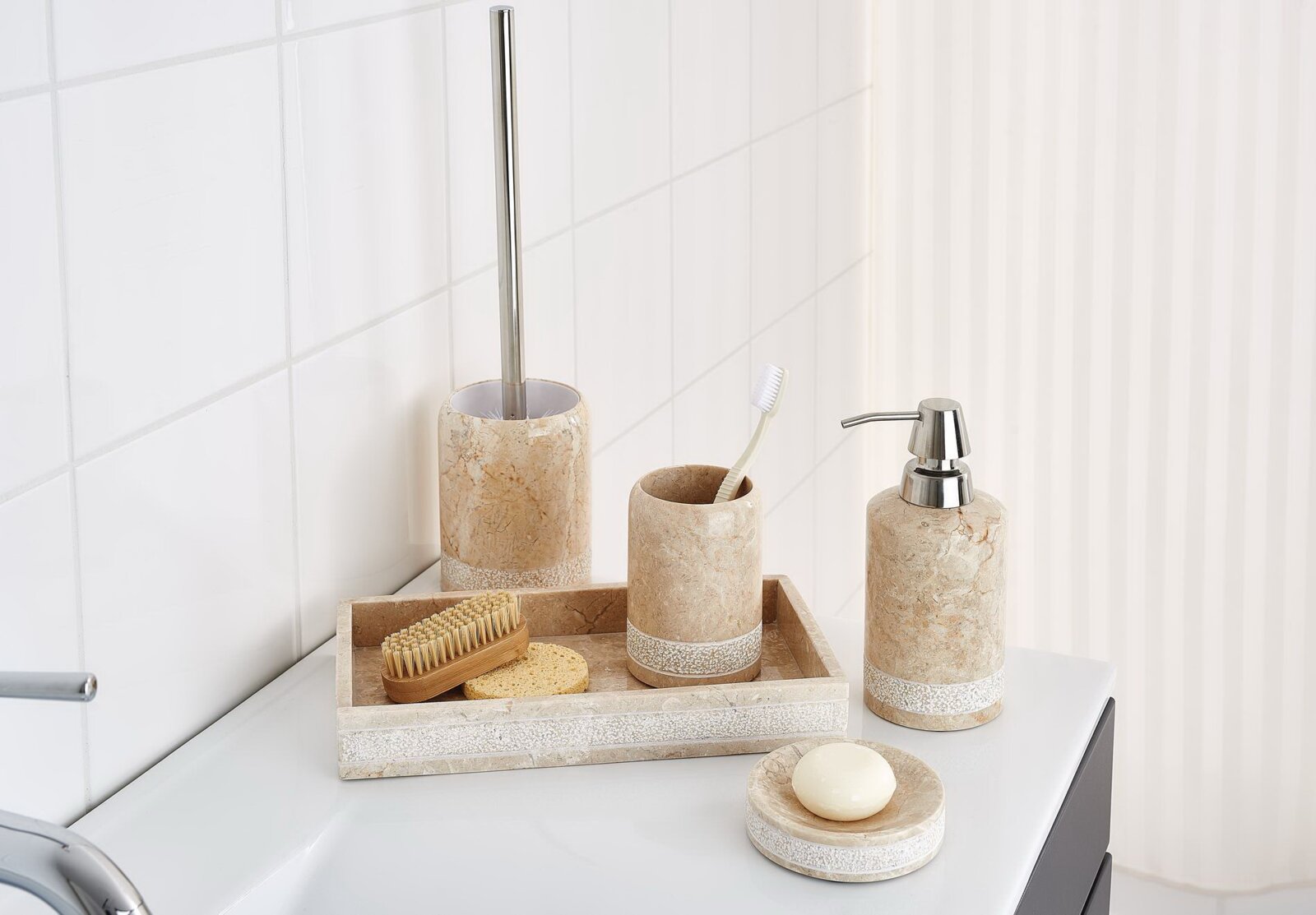 Beiges Badezimmer-Accessoire-Set in Steinoptik mit Seifenspender, Zahnputzbecher, WC-Bürstenhalter, Ablageschale und Seifenschale auf einem weißen Waschbecken, Perspektive: leicht schräg von vorne.