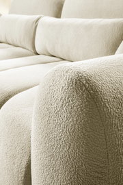 Nahaufnahme eines hellbeigen, weich strukturierten Sofas mit gepolsterter Armlehne und Rückenpolstern, fotografiert aus seitlicher Schrägperspektive.
