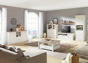 Helles Wohnzimmer mit einem weißen Sideboard im Landhausstil, frontal betrachtet, umgeben von weiteren passenden Möbeln und großen Fenstern.