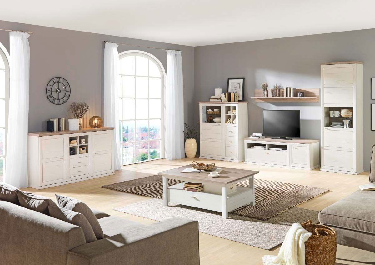 Helles Wohnzimmer mit einem weißen Sideboard im Landhausstil, frontal betrachtet, umgeben von weiteren passenden Möbeln und großen Fenstern.