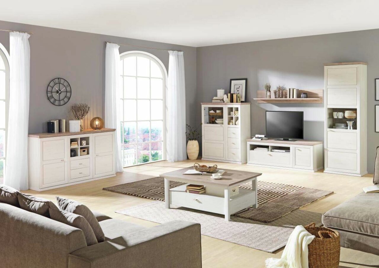 Helles Wohnzimmer mit einem weißen Sideboard im Landhausstil, frontal betrachtet, umgeben von weiteren passenden Möbeln und großen Fenstern.
