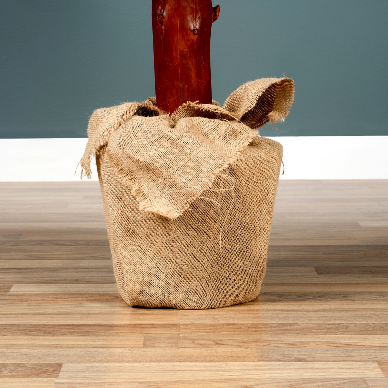 Nahaufnahme eines in Jute eingewickelten Baumstamms auf einem Holzboden, mit einem blauen Hintergrund.