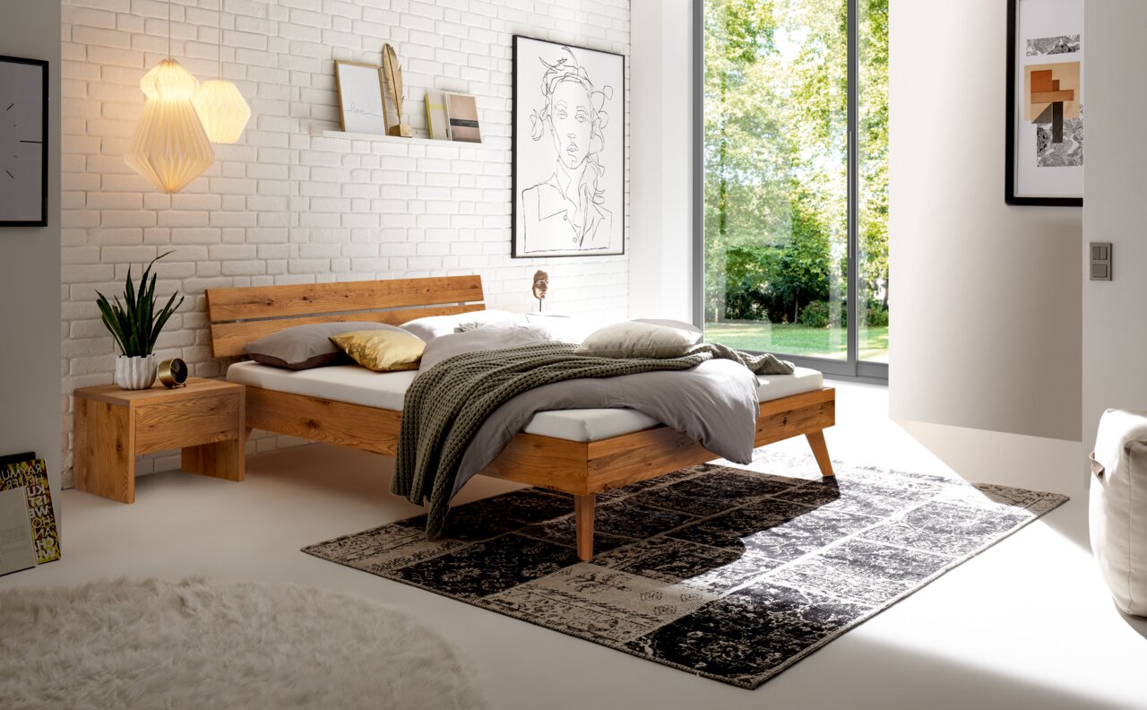 Modernes Schlafzimmer mit einem Kopfteil aus Holz und Metall, seitliche Perspektive, mit stilvoller Dekoration und großen Fenstern.