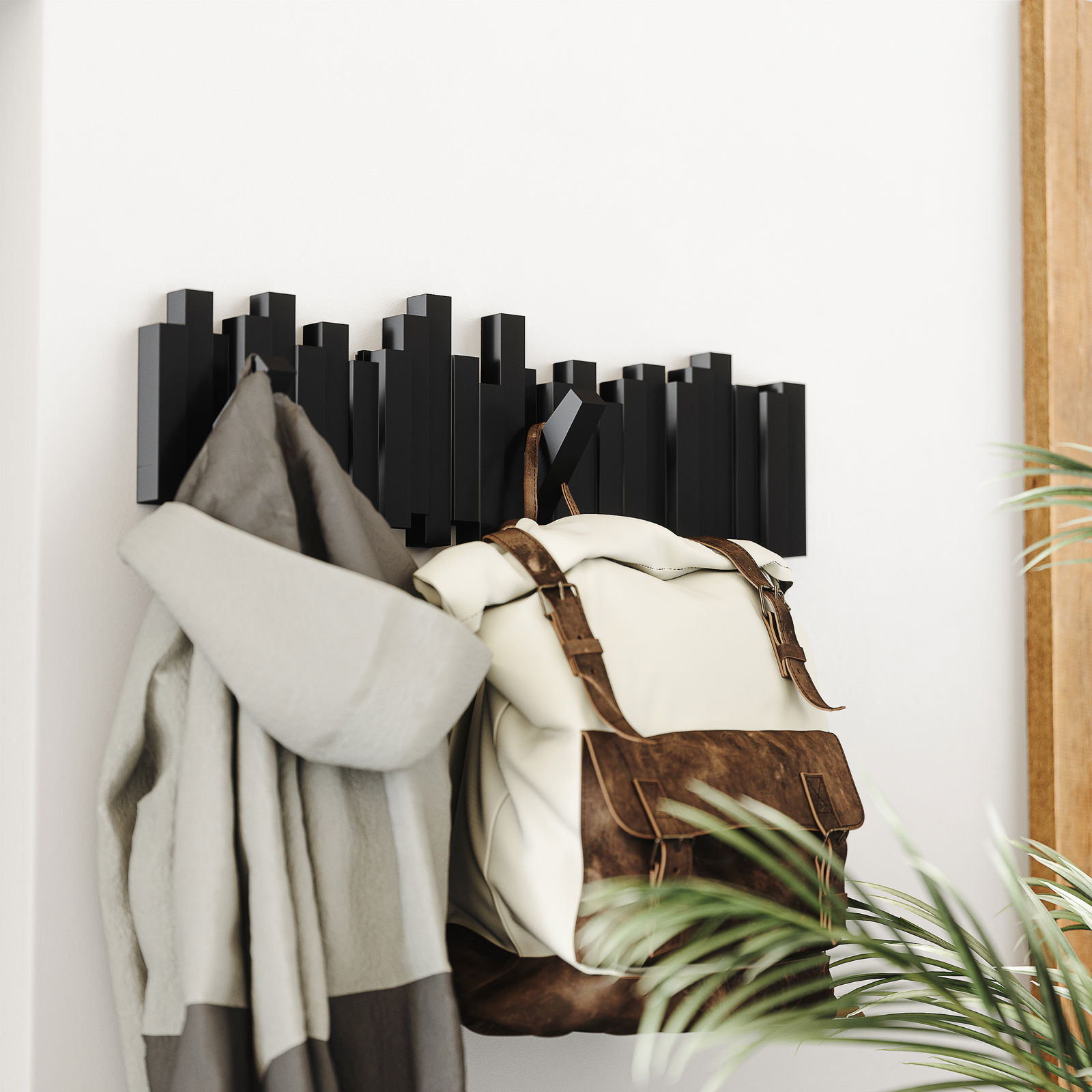 Moderne schwarze Wandgarderobe mit geometrischem Design, von der Seite betrachtet, mit aufgehängtem Mantel und Rucksack.