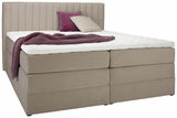 Beiges Boxspringbett mit gestepptem Kopfteil, seitlicher Blick, dekoriert mit lila Decke und Kissen.