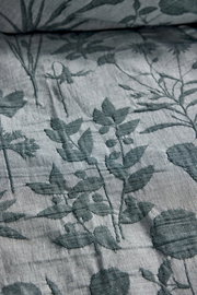 Nahaufnahme einer Bettwäsche mit floralem Muster in Grün auf grauem Hintergrund, perspektivisch von oben fotografiert.