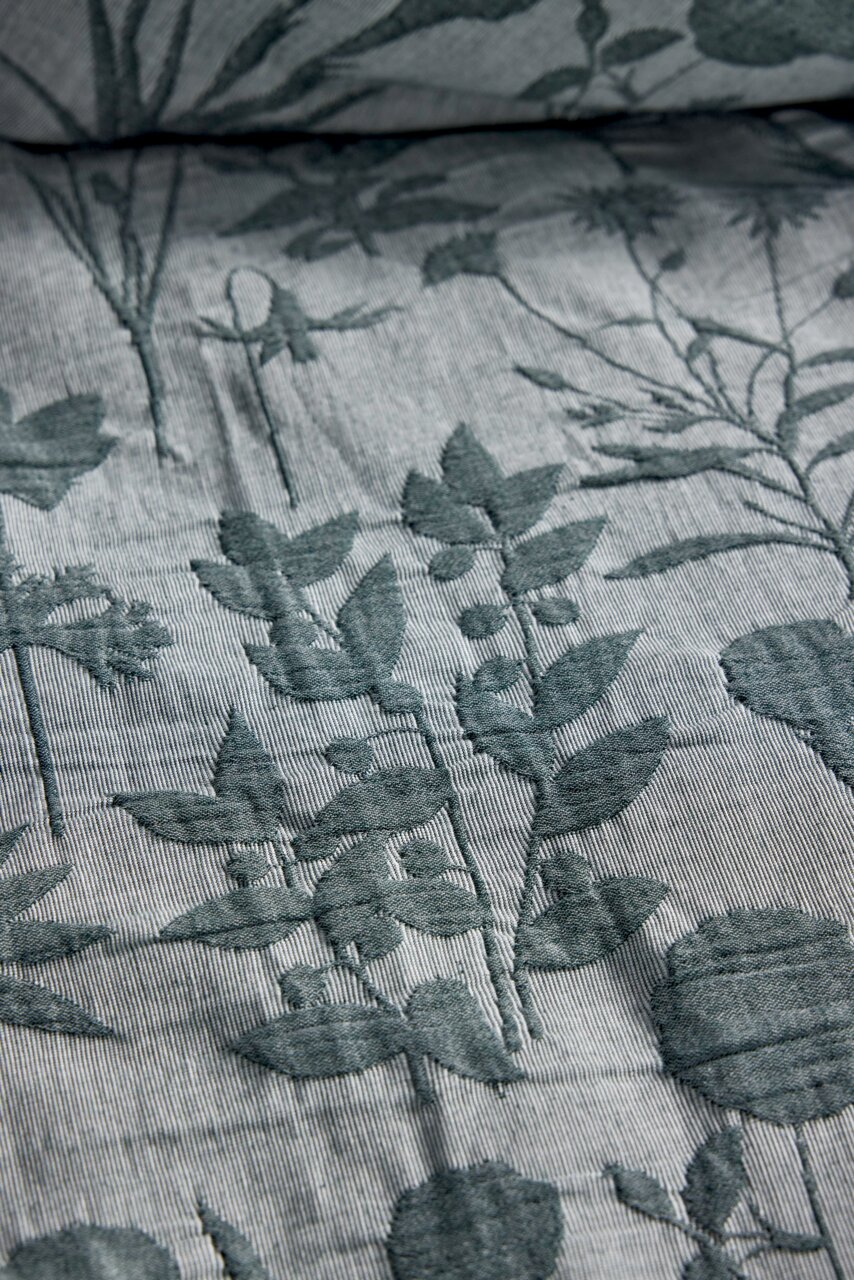 Nahaufnahme einer Bettwäsche mit floralem Muster in Grün auf grauem Hintergrund, perspektivisch von oben fotografiert.