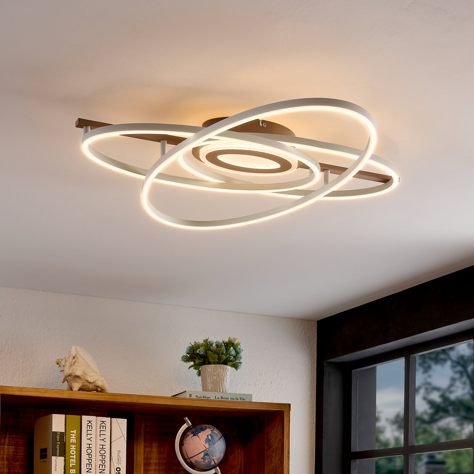 Novel LED-plafondlamp Moderne LED plafondlamp met overlappende ovale ringen in wit met warm wit licht, gemonteerd aan het plafond; perspectief van onderaf (kijk omhoog) in een interieur.