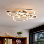 Moderne LED plafondlamp met overlappende ovale ringen in wit met warm wit licht, gemonteerd aan het plafond; perspectief van onderaf (kijk omhoog) in een interieur.